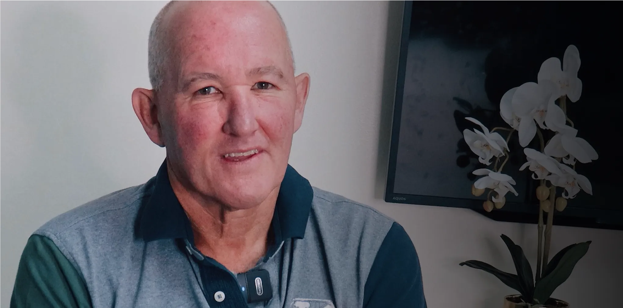 A man in a grey and green shirt is smiling.