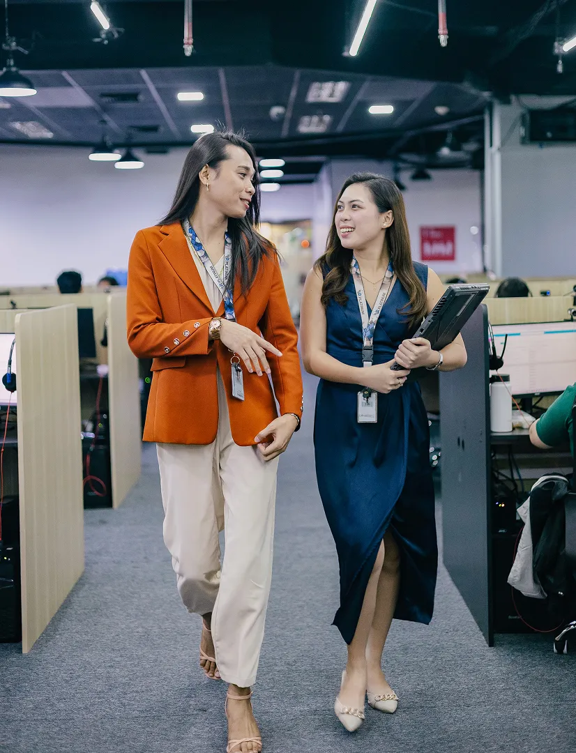 Two women are talking in an office cubicle.