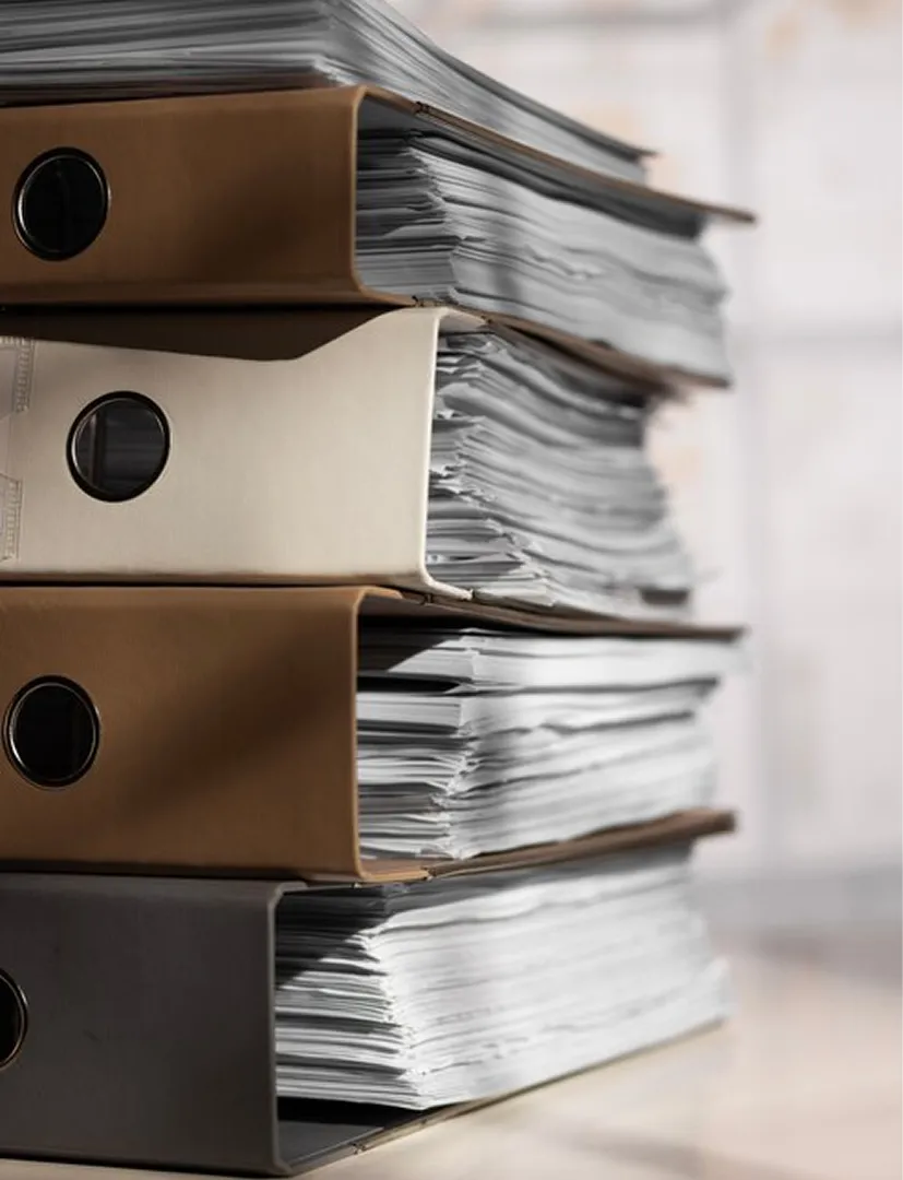 Stack of four thick binders filled with large amounts of paper on a desk.
