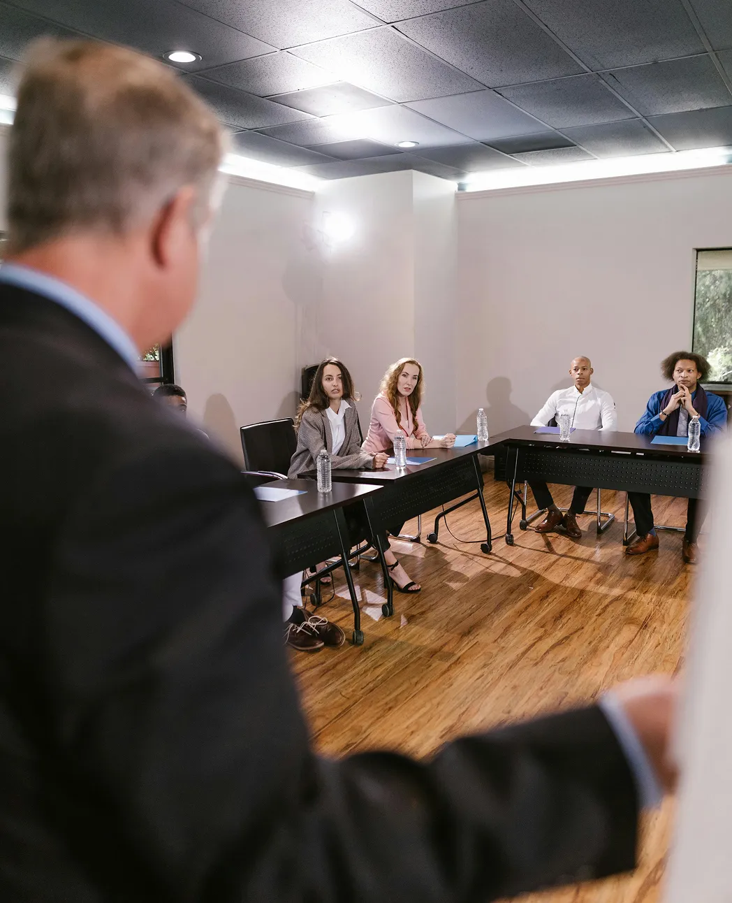 Four people sitting at conference tables listening to a man speaking in a meeting room.