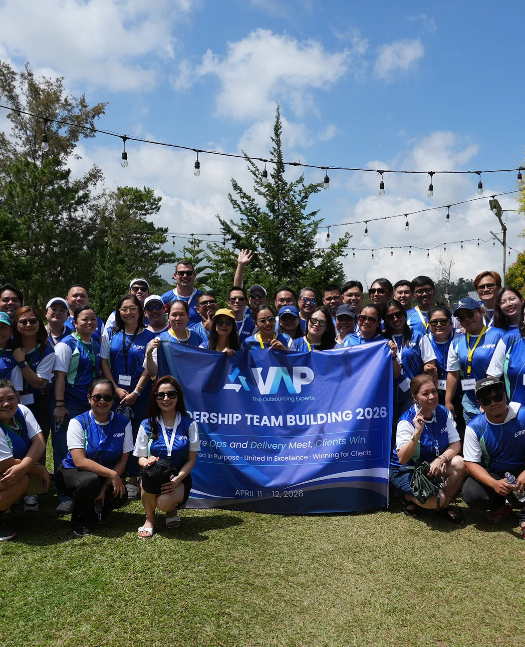 Large group wearing blue shirts posing outdoors holding a banner for VAP Leadership Team Building 2026.