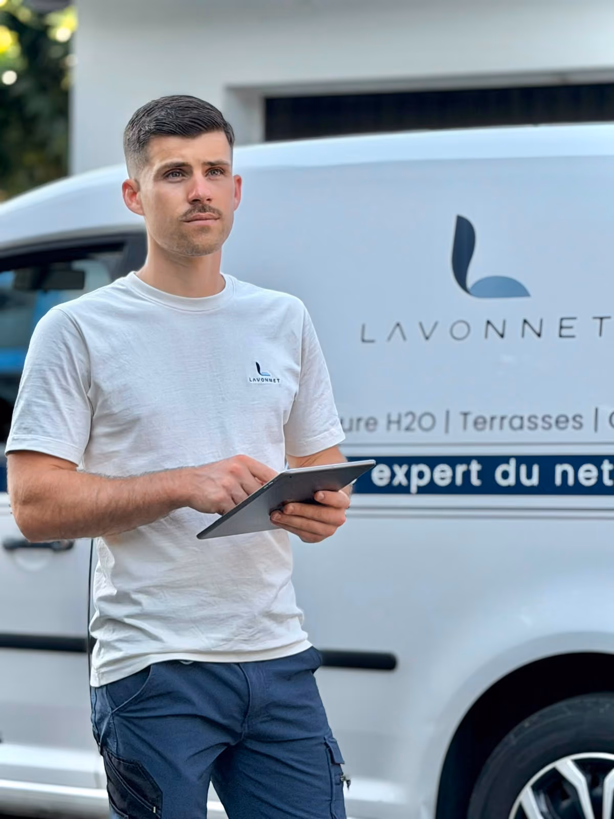 Homme en t-shirt blanc avec logo Lavonnet utilise une tablette devant une camionnette de service.