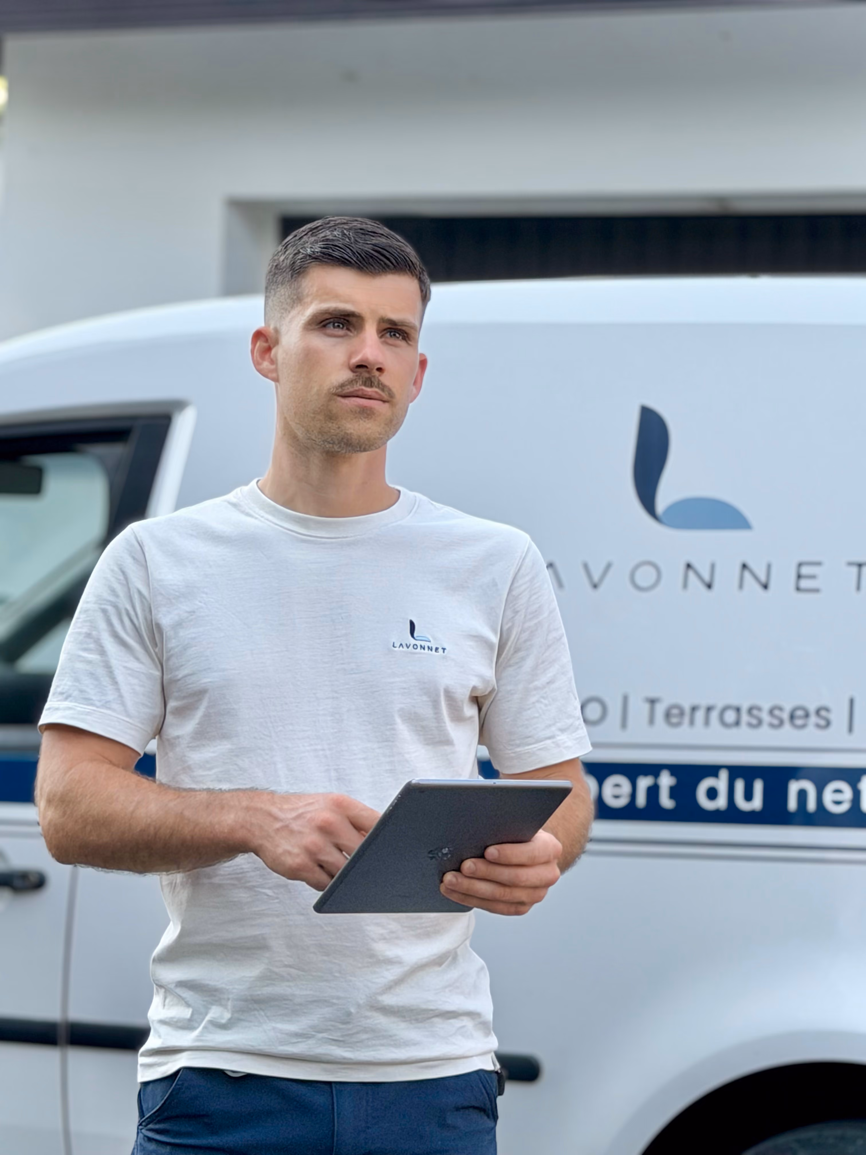 Homme en t-shirt blanc avec logo Lavonnet utilise une tablette devant une camionnette de service.