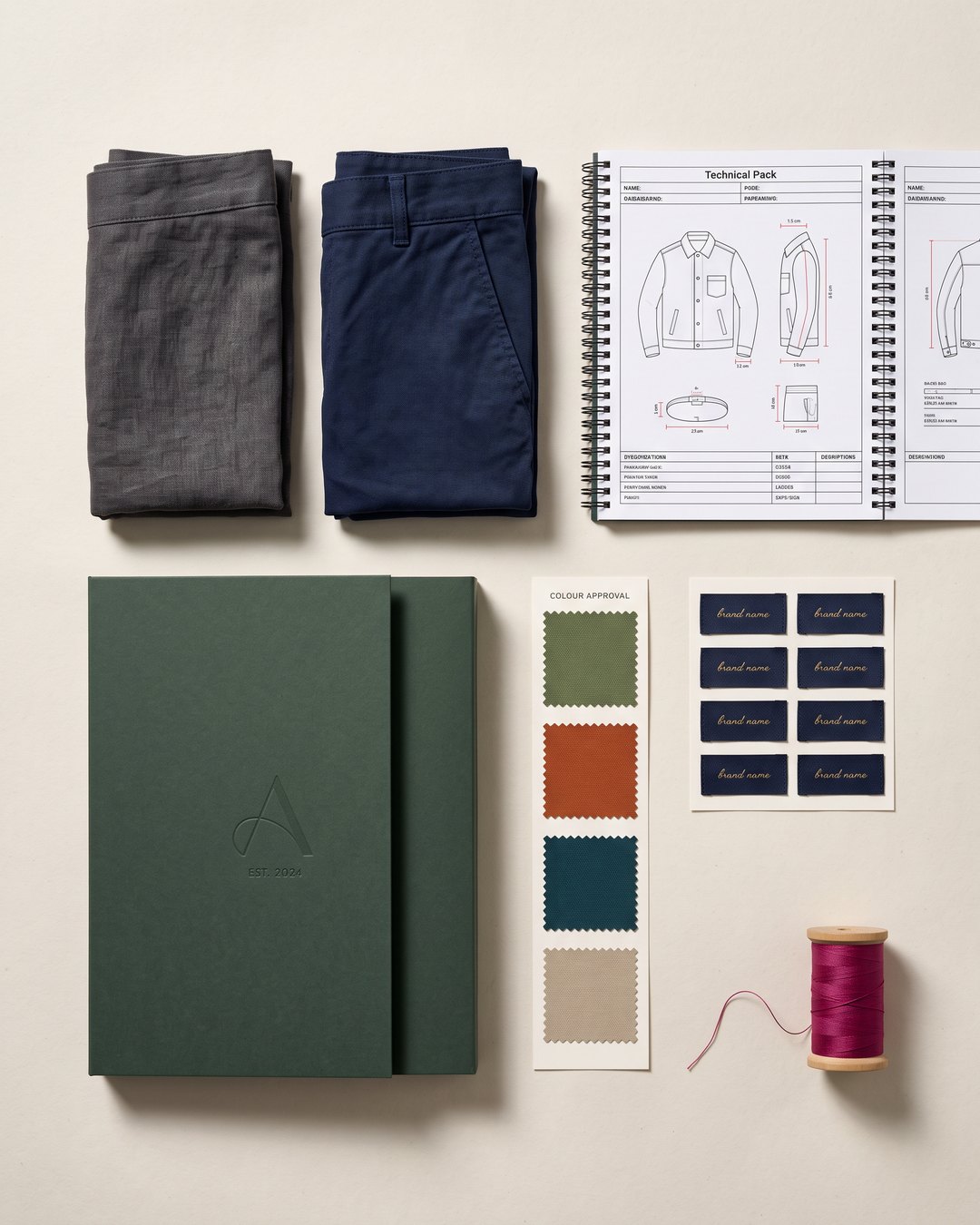 Garment samples, a tech pack, fabric colour dips and custom woven labels laid out for a properly resourced brand launch
