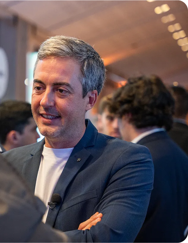 Nicolas Chéron, bras croisés et micro-cravate fixé au revers, échangeant dans une ambiance de networking pendant un salon.