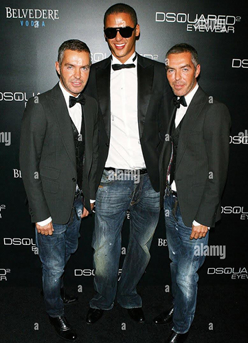 Simo-Azzaoui und zwei Männer in schwarzen Anzügen mit Fliegen und Jeans posieren vor einer Werbewand.