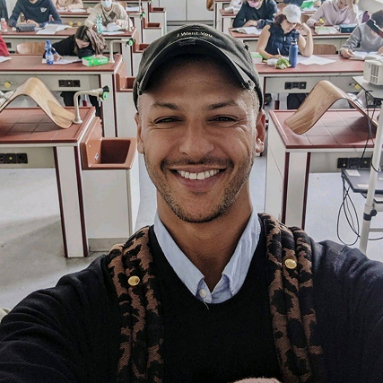 Simo Azzaoui mit schwarzer Kappe macht ein Selfie in einem Klassenzimmer mit mehreren Schülern im Hintergrund.