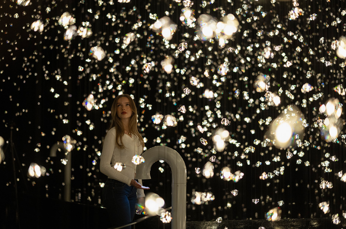 In der immersiven Wunderkammer Pulse Voronoi der Swarovski Kristallwelten steht eine junge Frau, umgeben von tausenden funkelnden Kristallen.