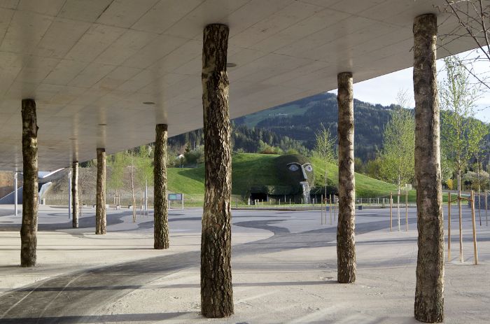 Foyer der Swarovski Kristallwelten mit Betondecke, die von naturbelassenen Baumstämmen getragen wird. Durch die Säulen öffnet sich der Blick auf die Parklandschaft mit dem ikonischen Riesen.