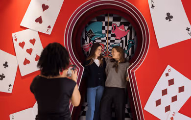 Disney photo spot at Swarovski Kristallwelten Store Wattens — two visitors pose in an Alice in Wonderland scene with oversized playing cards and a key motif.