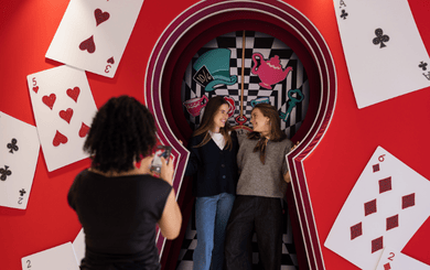 Disney Fotospot im Swarovski Kristallwelten Store Wattens – zwei Besucherinnen posieren in einer Alice-im-Wunderland-Szene mit überdimensionalen Spielkarten und Schlüsselmotiv.