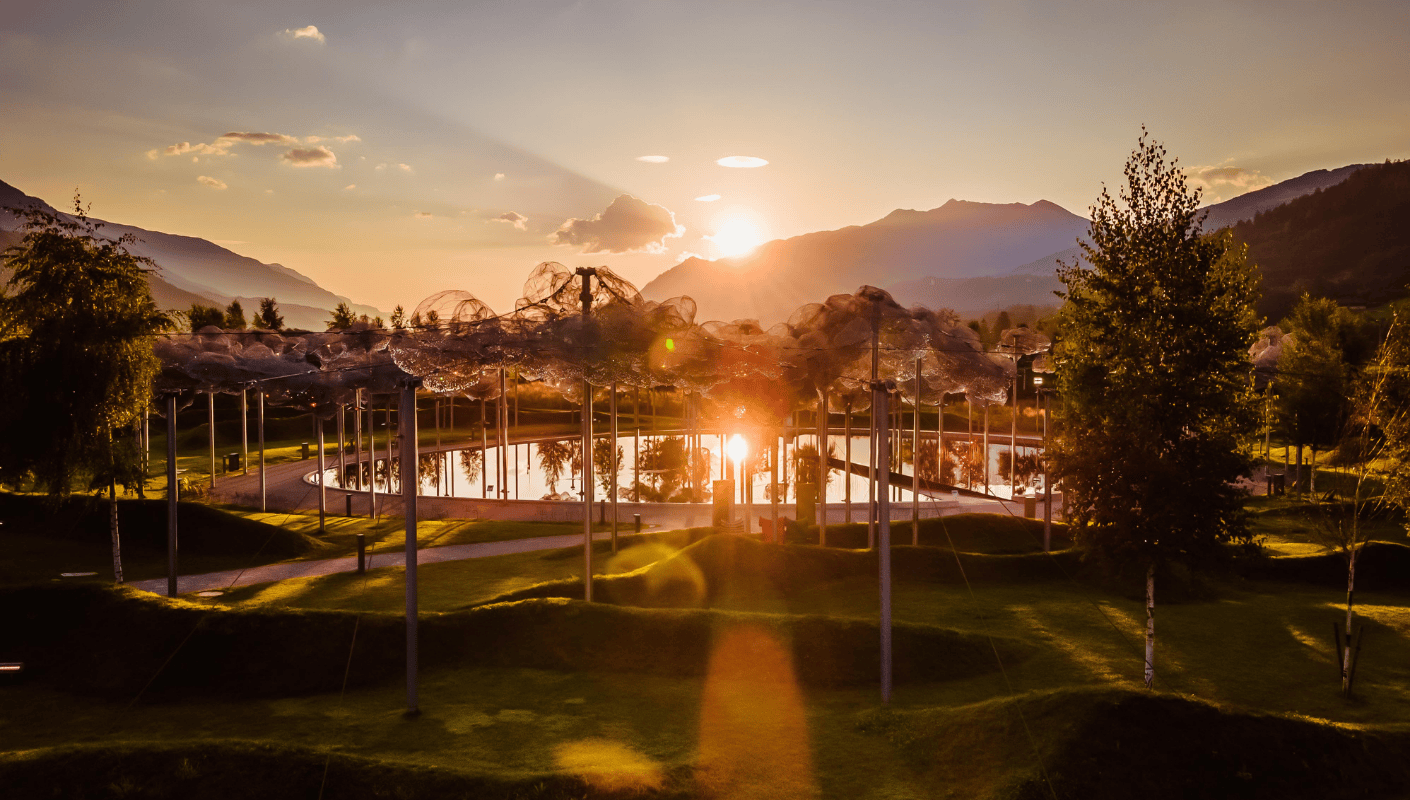 The crystal cloud in the park of Swarovski Kristallwelten at sunset — sparkling crystal clouds are reflected in black mirror water, surrounded by a gentle mountain landscape.