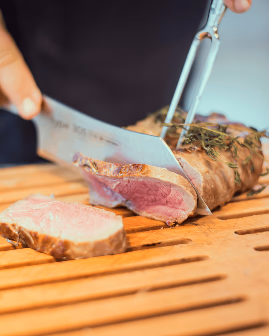 Juicy pink fried meat is sliced by a chef on a wooden board.