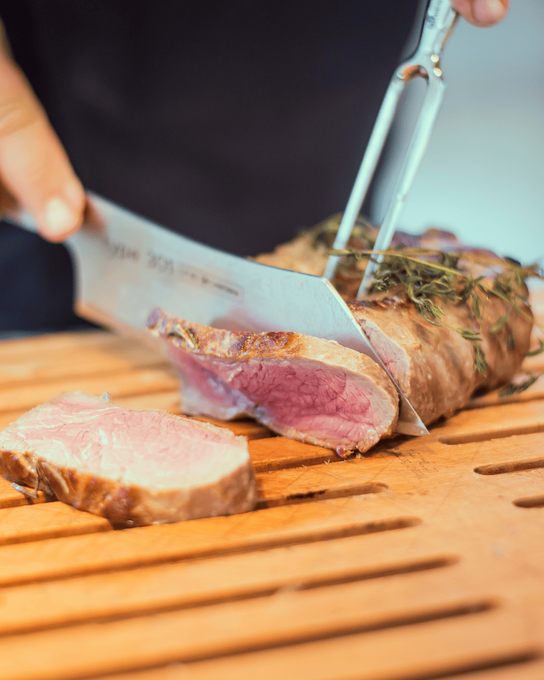 Juicy pink fried meat is sliced by a chef on a wooden board.