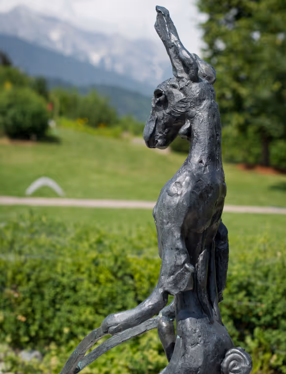 A detailed bronze sculpture of a hare stands in the countryside. The figure appears artistically abstract and is part of the diverse art installations in the park of Swarovski Kristallwelten.