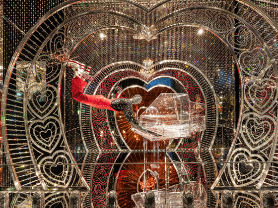 Nachgebildete Figur von Elton John, schwebend in rotem Anzug mit funkelndem Cape vor einem Kristallflügel, umrahmt von Herzornamenten und tausenden Kristallen in der Wunderkammer Art of Performance in den Swarovski Kristallwelten