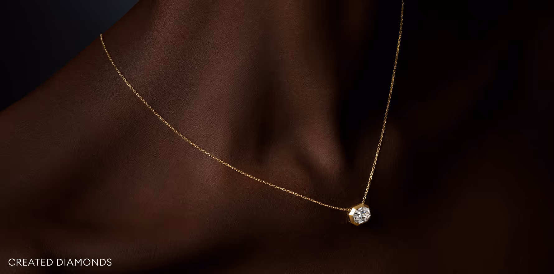 Fine gold necklace with a Swarovski Created Diamond pendant, worn on the neck, set against a dark background.