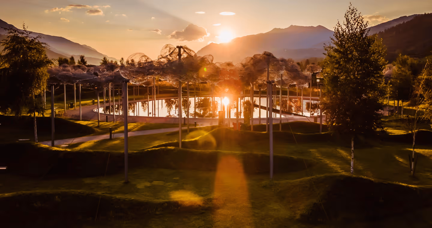 The crystal cloud in the park of Swarovski Kristallwelten at sunset — sparkling crystal clouds are reflected in black mirror water, surrounded by a gentle mountain landscape.