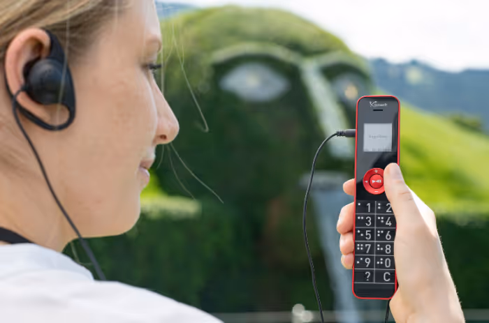 Visitor with headphones holds an audio guide player, in the background the giant with a waterfall at Swarovski Kristallwelten.
