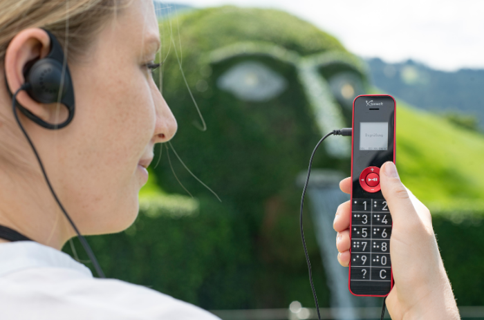 Besucherin mit Kopfhörern hält einen Audioguide-Player in der Hand, im Hintergrund der Riese mit Wasserfall in den Swarovski Kristallwelten.