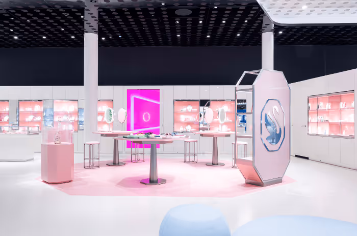 Interior view of the Swarovski Crystal Worlds Store in Wattens: modern retail space with white furniture, pink accents, glowing presentation islands and display cases full of jewelry.