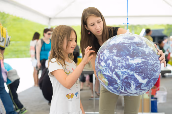 Adults show a child a big globe at a Swarovski Water School hands-on station — learning about water and the environment through play.