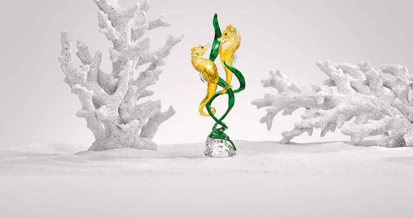 Sparkling Swarovski crystal figure with two seahorses, artfully entwined in green algae, presented in an underwater world with a white coral reef.
