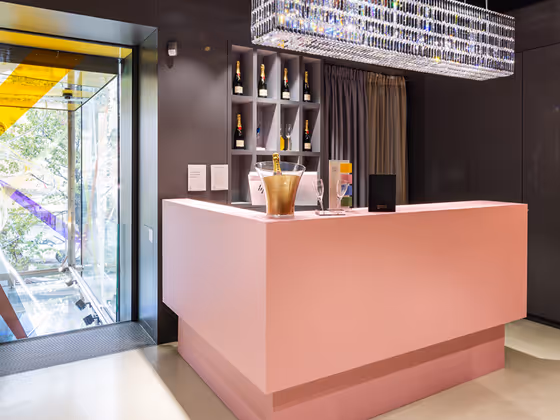 Moët & Chandon Bar im Swarovski Kristallwelten Store Wien mit rosa Theke, Champagnerflaschen im Regal und funkelndem Kristallluster.