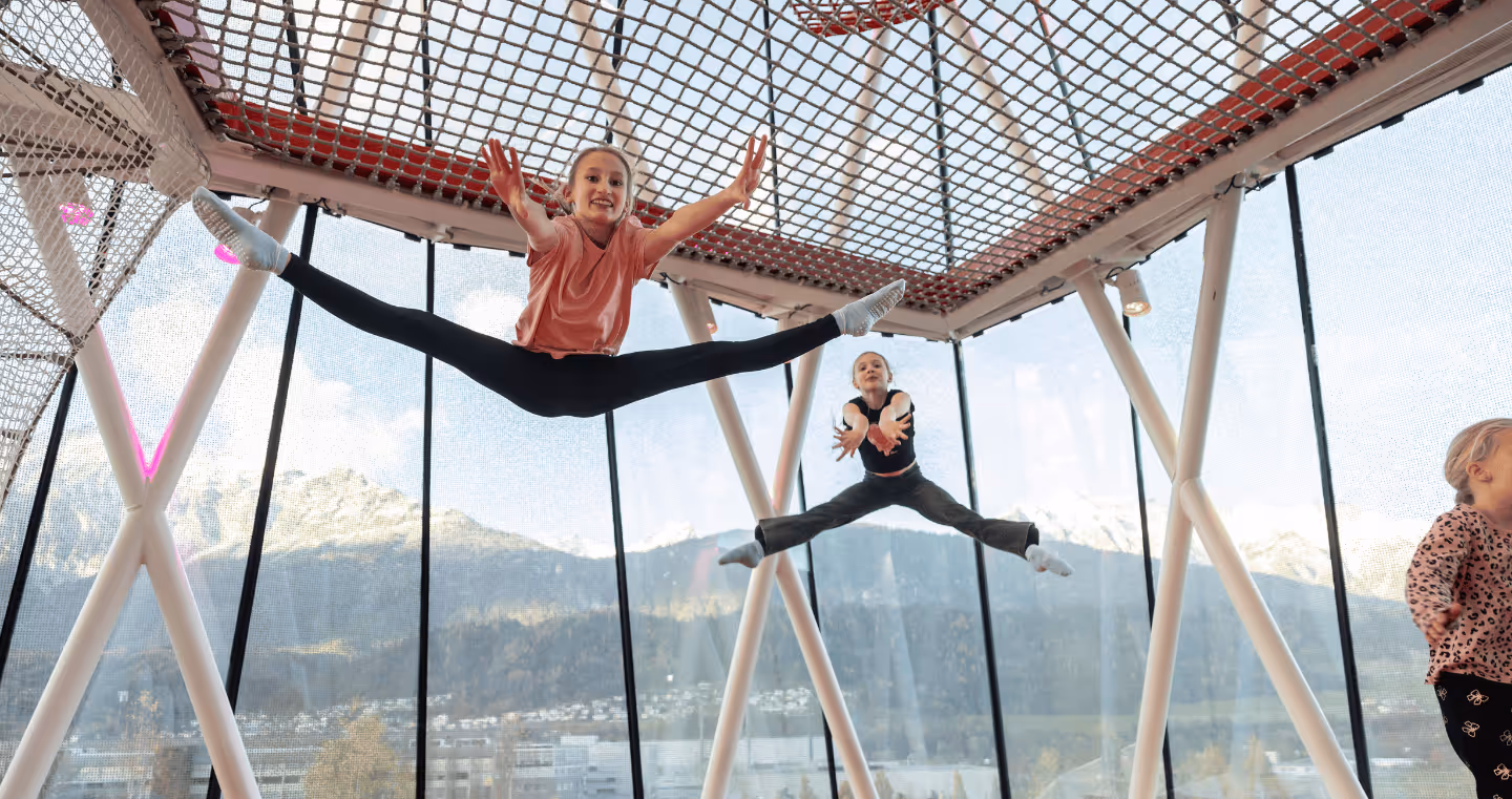 Children jump and frolic in the play tower of Swarovski Kristallwelten — movement and fun with a Tyrolean mountain panorama in the background.