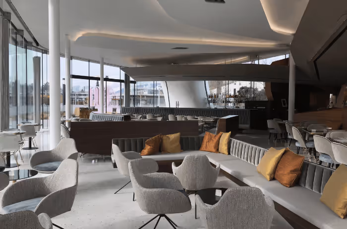 Modern interior of the Daniels Kristallwelten by DoN restaurant at Swarovski Kristallwelten: bright, open architecture with large glass fronts, elegant grey armchairs and sofas with gold and bronze cushions.