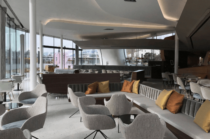 Modernes Interieur des Restaurants Daniels Kristallwelten by DoN in den Swarovski Kristallwelten: helle, offene Architektur mit großen Glasfronten, eleganten grauen Sesseln und Sofas mit gold- und bronzefarbenen Kissen.