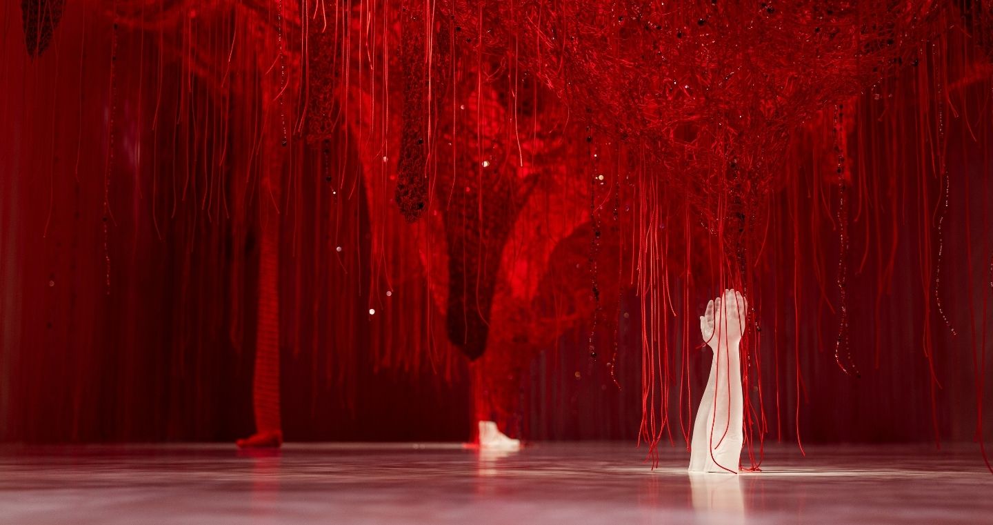 Wunderkammer Crystallizing Identity von Chiharu Shiota in den Swarovski Kristallwelten: Ein dichtes Netz aus roten Fäden mit eingearbeiteten Kristallen, aus dem eine weiße Kristallhand emporragt.