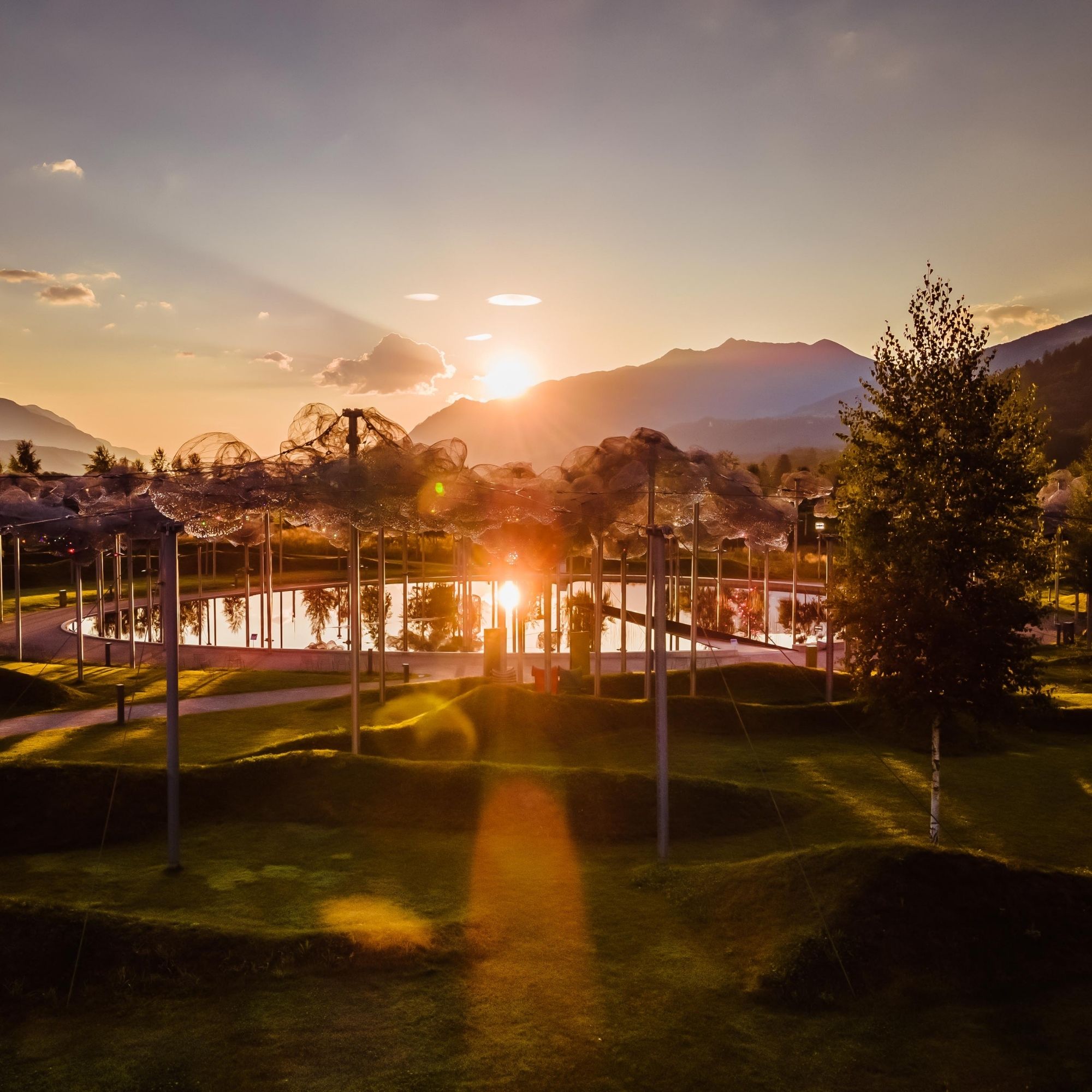 Die Kristallwolke in den Swarovski Kristallwelten bei Sonnenuntergang – funkelnde Wolken aus Kristall spiegeln sich im schwarzem Spiegelwasser, umgeben von sanfter Berglandschaft.