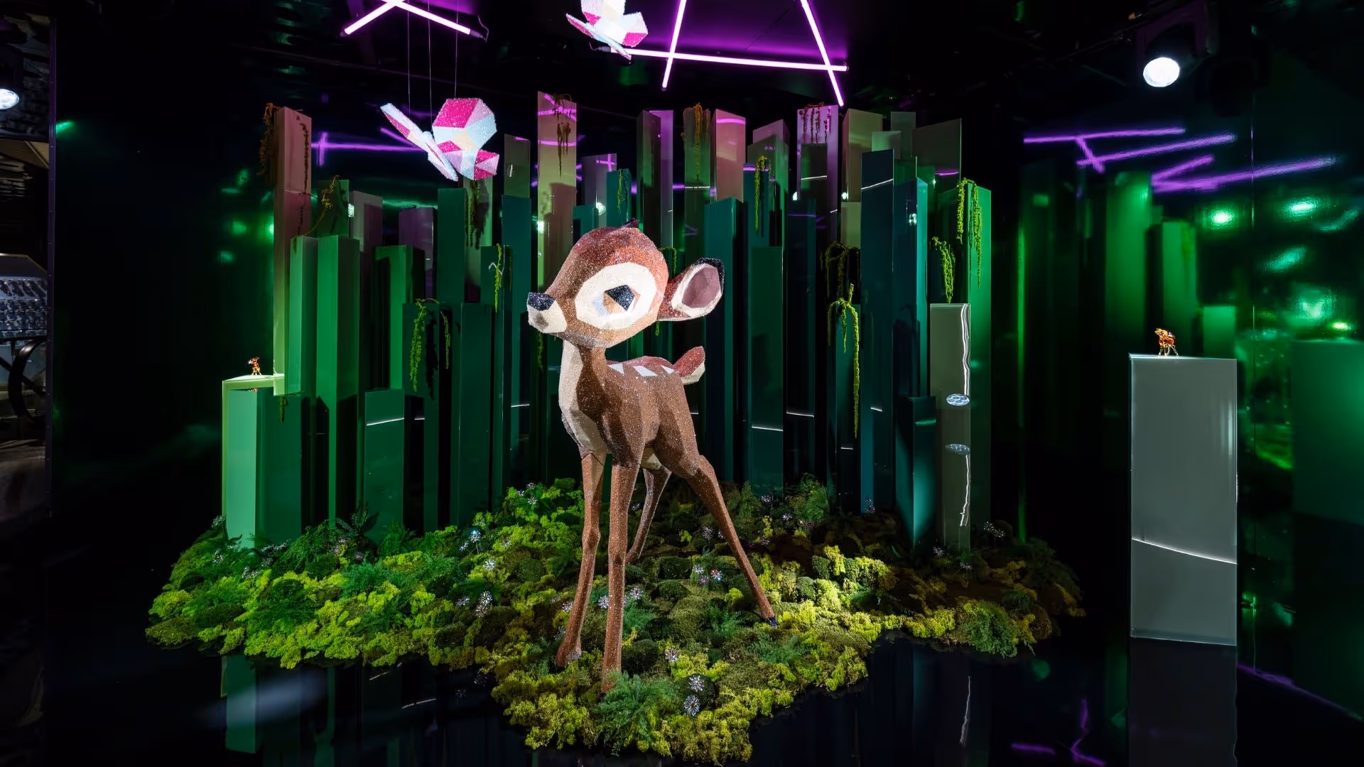 Crystal figure of Disney's Bambi in the Swarovski Kristallwelten Store Wien — artistic presentation with sparkling crystals, green forest landscape, lighting effects and crystal butterflies.