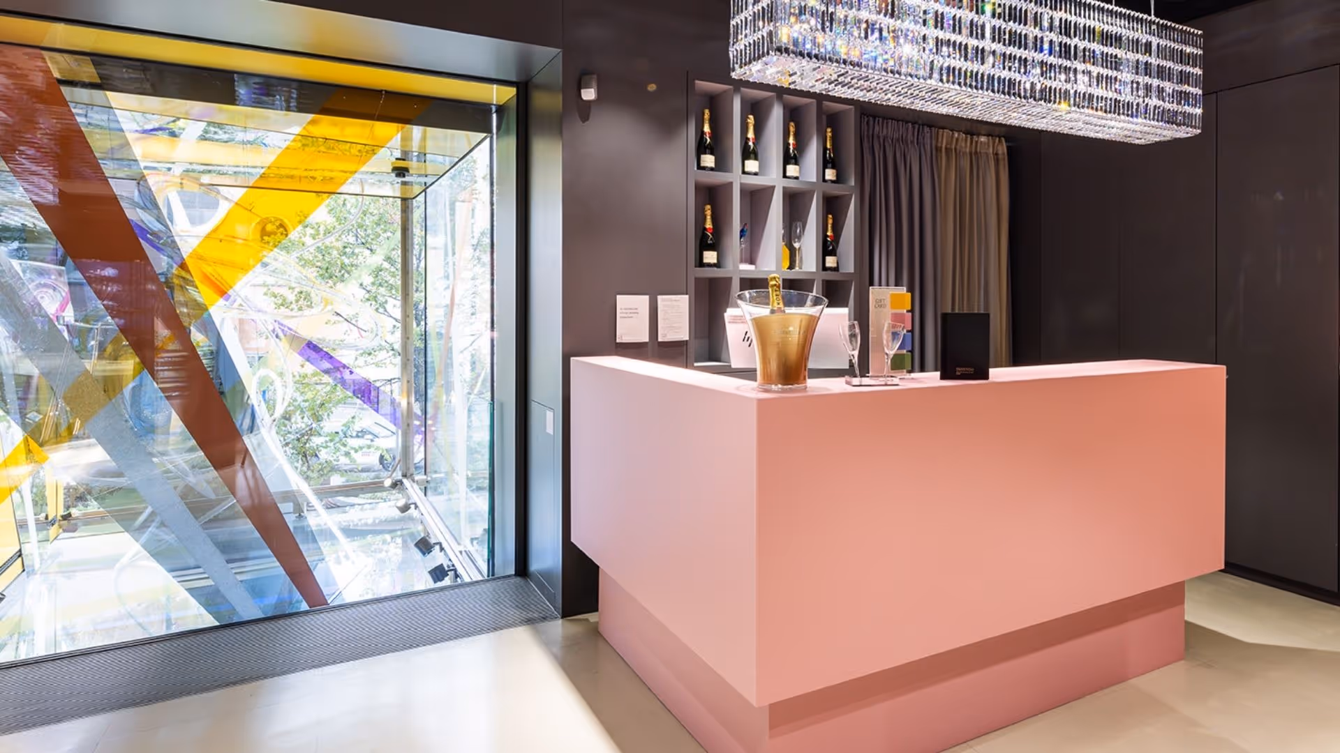 Moët & Chandon Bar in the Swarovski Kristallwelten Store Wien with pink bar, champagne bottles on the shelf and sparkling crystal chandelier.