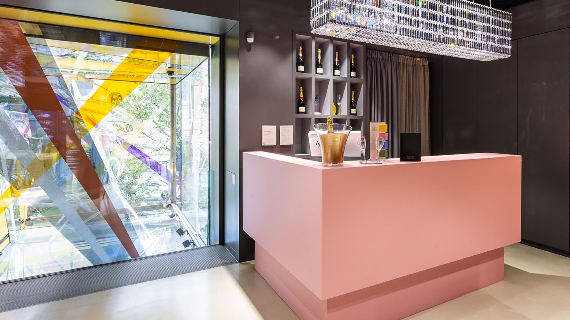 Moët & Chandon Bar in the Swarovski Kristallwelten Store Wien with pink bar, champagne bottles on the shelf and sparkling crystal chandelier.