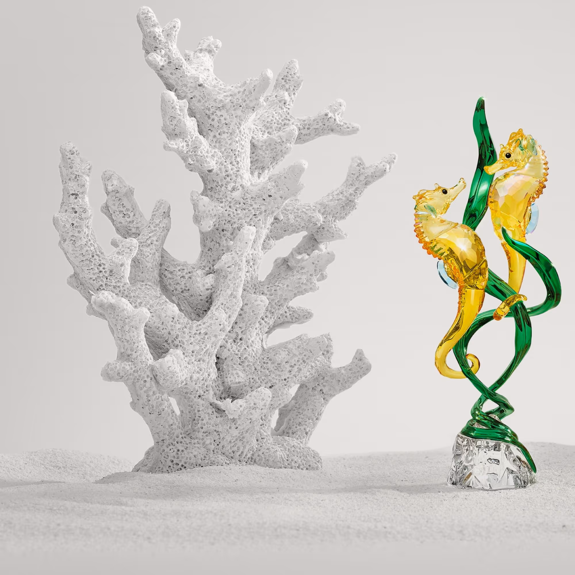 Sparkling Swarovski crystal figure with two seahorses, artfully entwined in green algae, presented in an underwater world with a white coral reef.