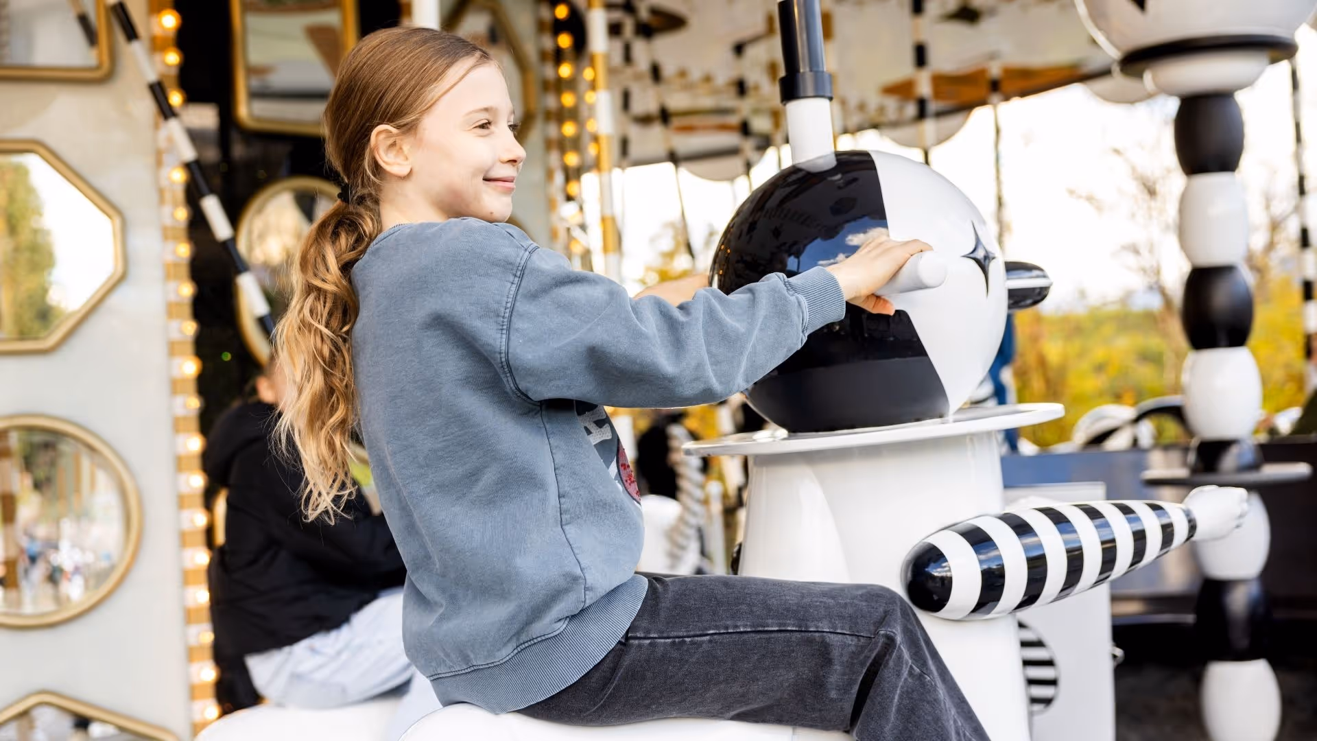 Girl sits smiling on the artfully designed black and white carousel in the park of Swarovski Kristallwelten.