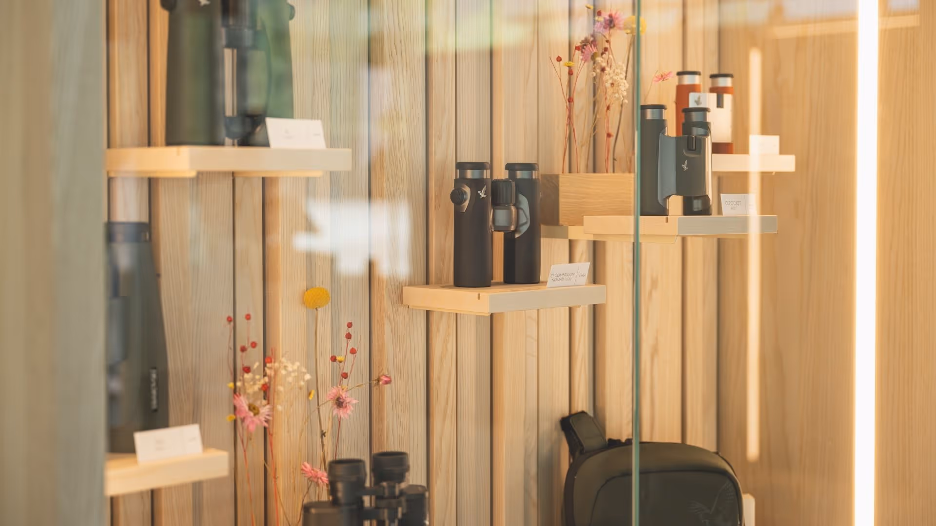 Exhibition of binoculars at the Swarovski Optik Store at Swarovski Kristallwelten — elegant wooden shelves with various models, complemented by subtle floral arrangements.