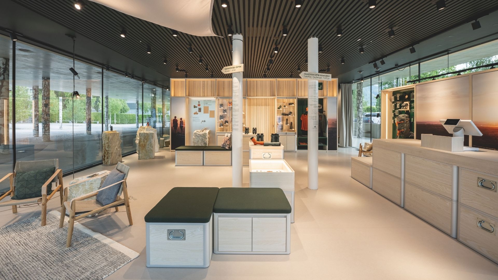 Innenansicht des Swarovski Optik Stores in den Swarovski Kristallwelten mit modernem, naturverbundenem Design, großen Glasfronten, Sitzgelegenheiten und Präsentationsflächen für Ferngläser und Zubehör.