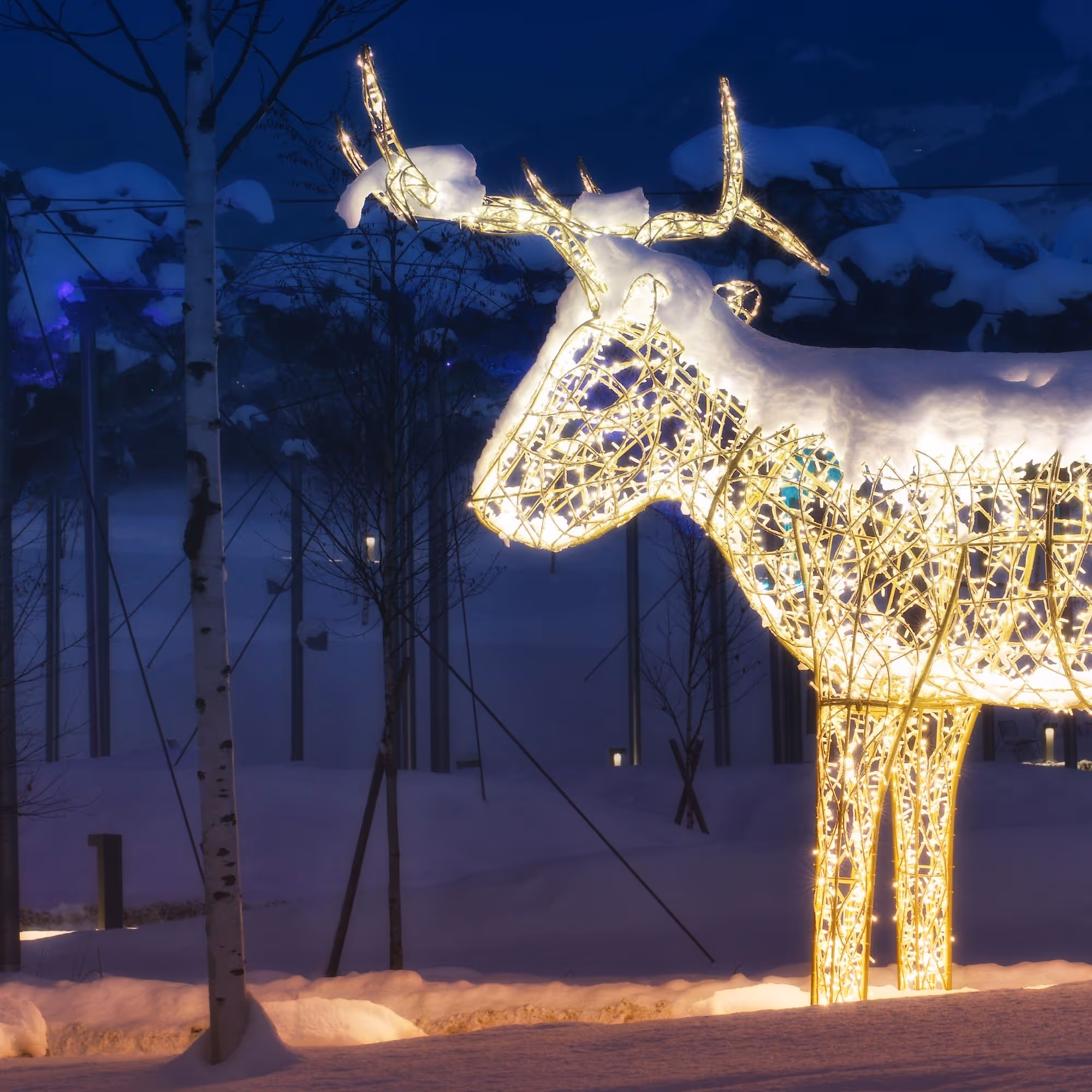 Schneebedeckte, illuminierte Rentierfigur leuchtet in der verschneiten Winterlandschaft des Winter Wonderland der Swarovski Kristallwelten.