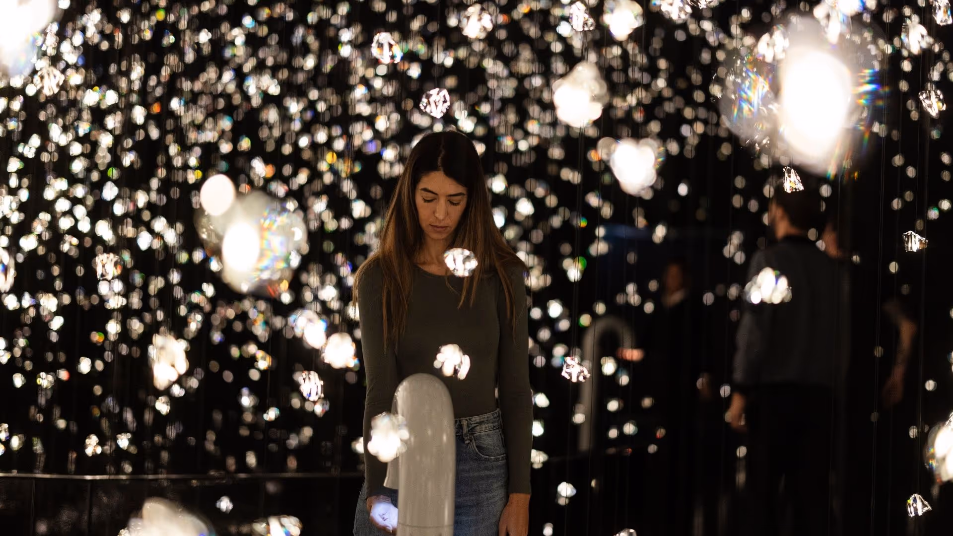 Eine junge Frau steht in der immersiven Wunderkammer Pulse Voronoi, umgeben von tausenden funkelnden Kristallen in den Swarovski Kristallwelten.
