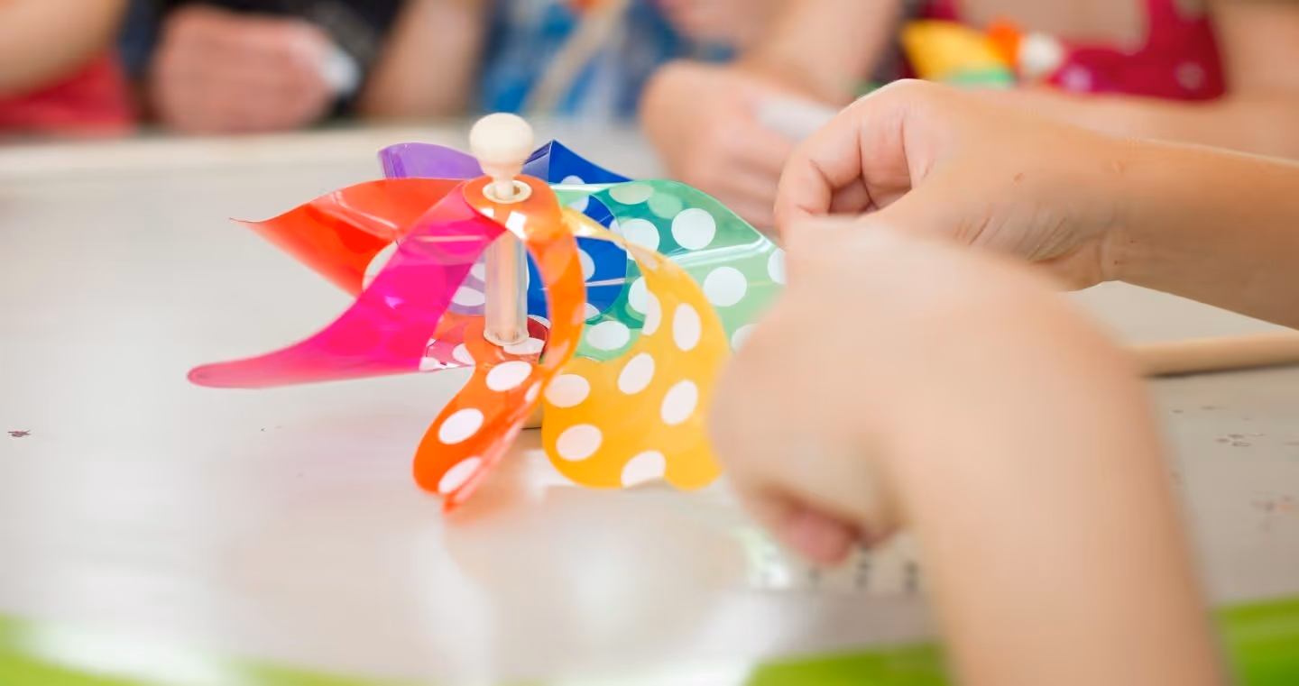 Children's hands make a colorful wind turbine with white dots during a children's program at Swarovski Kristallwelten.