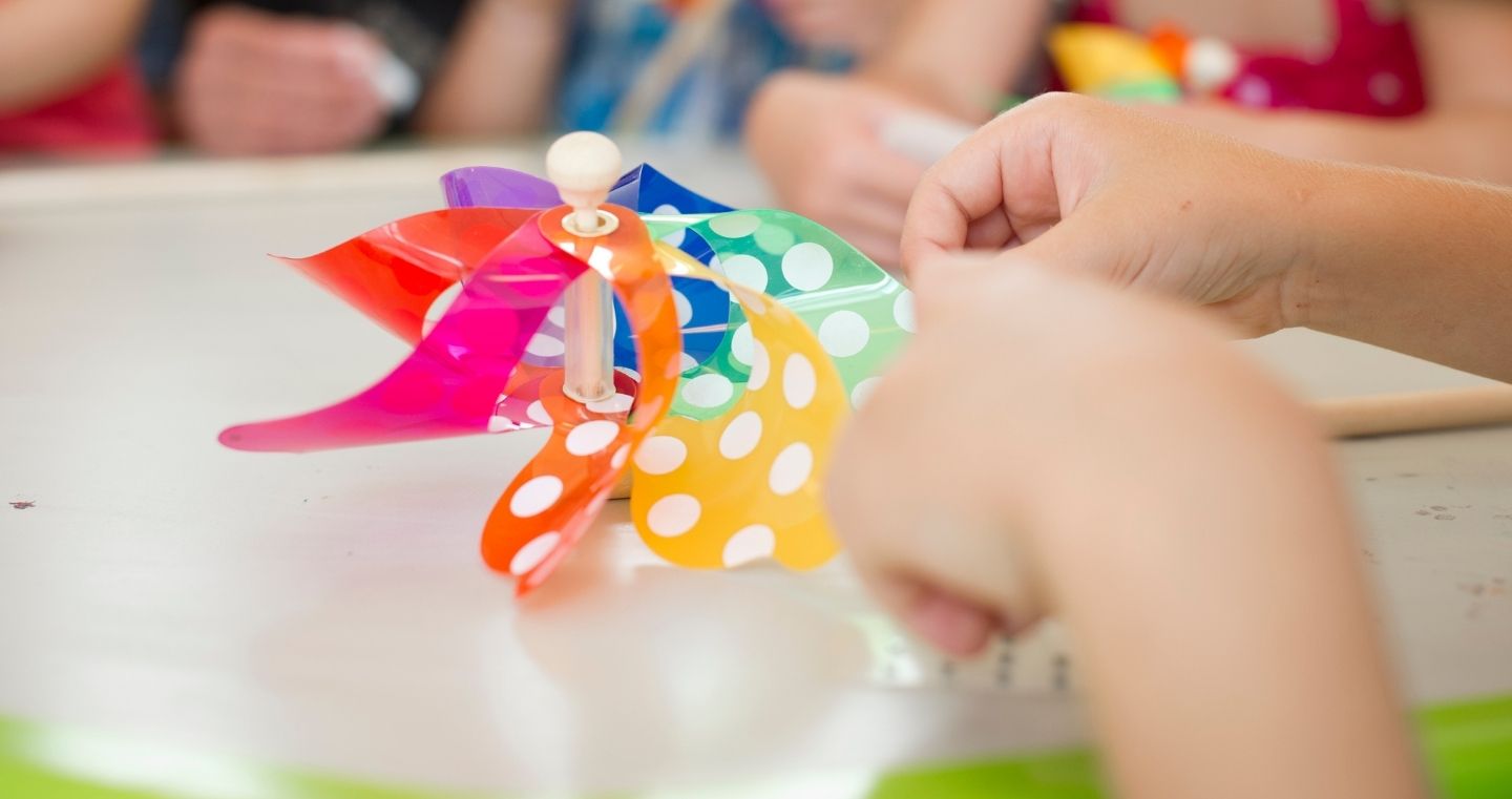 Kinderhände basteln ein buntes Windrad mit weißen Punkten während eines Kinderprogramms in den Swarovski Kristallwelten.