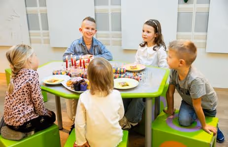 Group of children celebrate together at the table with muffins and candles as part of a Swarovski Kristallwelten birthday program.