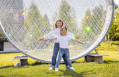 Two children pose laughing with outstretched arms in front of the sparkling work of art Prologue III in the Park — The Giant Birthday Party, birthday program at Swarovski Kristallwelten.