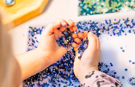 A child holds a variety of sparkling Swarovski crystals in shades of blue and green with both hands — creative birthday program “Crystal Detectives in Action” at Swarovski Kristallwelten.