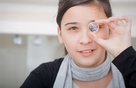 Schoolgirl looks through sparkling Swarovski crystal — museum educational student program at Swarovski Kristallwelten.