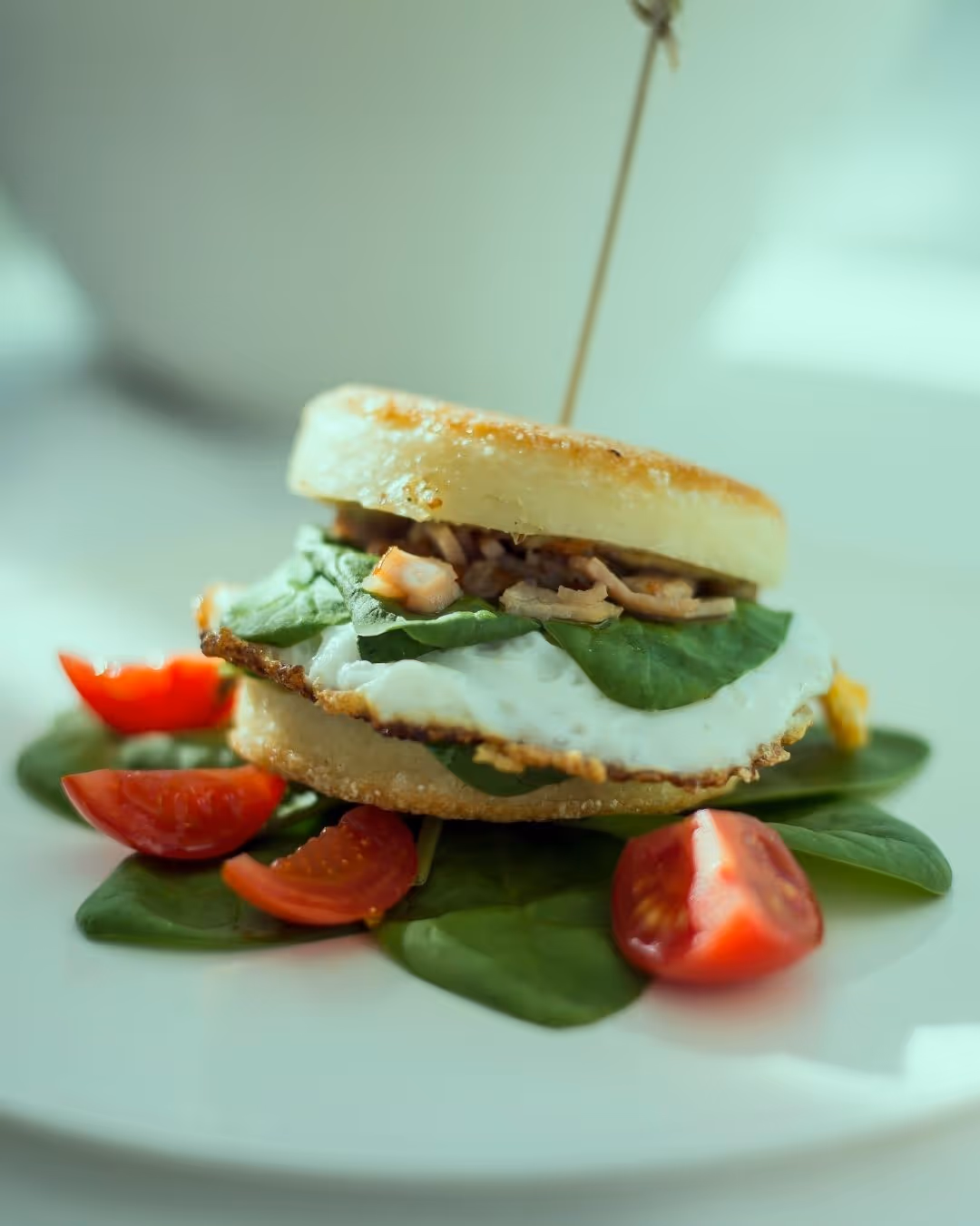 Fresh bagel burger with spinach, fried eggs and chicken pieces served with cherry tomatoes on a white plate at Daniels Kristallwelten by DoN restaurant.