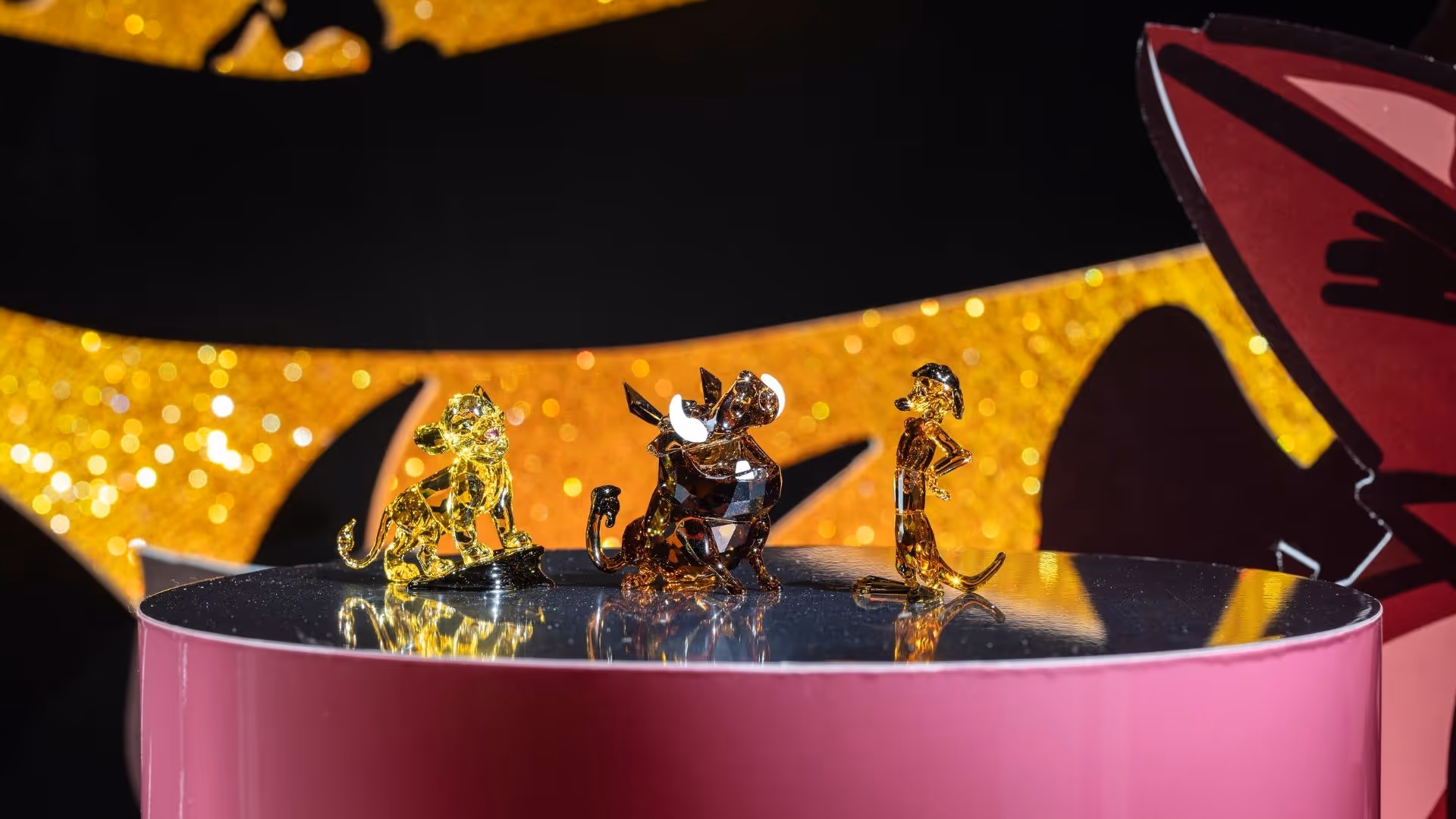 Disney x Swarovski Kunstbühne im Swarovski Kristallwelten Store Wattens – funkelnde Kristallfiguren von Simba, Timon und Pumbaa vor golden Hintergrund.